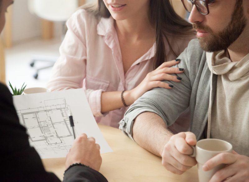 Close up of millennial couple visiting architect or designer office, consulting about future house project, young spouses deciding to buy first apartment or flat together or planning home renovation.